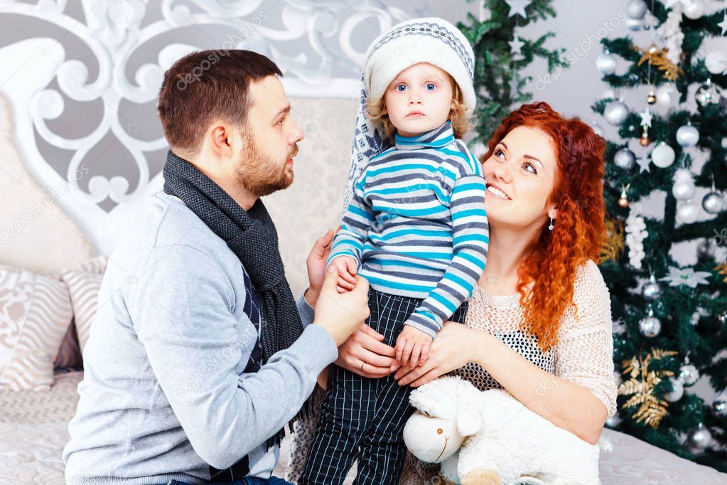Christmas happy family of three persons and fir tree with gift boxes over white bedroom background