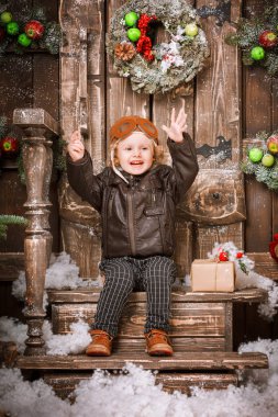 Neşeli mutlu küçük iki yaşında bir çocuk braun deri ceket, pantolon ve bot üzerinde Noel süslemeleri poz pilot şapkası giymiş