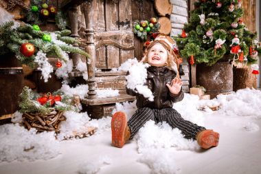 Braun deri ceket, pantolon ve bot üzerinde ahşap dekorasyon kar ile oyunlarında Noel poz pilot şapkası ile küçük iki yaşında bir çocuk giymiş