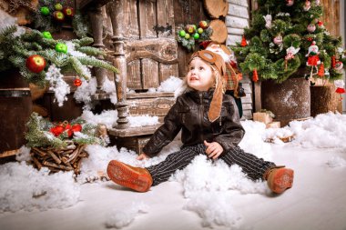 Braun deri ceket, pantolon ve bot üzerinde ahşap dekorasyon kar ile oyunlarında Noel poz pilot şapkası ile küçük iki yaşında bir çocuk giymiş