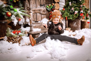 Braun deri ceket, pantolon ve bot üzerinde ahşap dekorasyon kar ile oyunlarında Noel poz pilot şapkası ile küçük iki yaşında bir çocuk giymiş