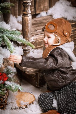 Braun deri ceket, pantolon ve bot üzerinde ahşap dekorasyon kar ile oyunlarında Noel poz pilot şapkası ile küçük iki yaşında bir çocuk giymiş