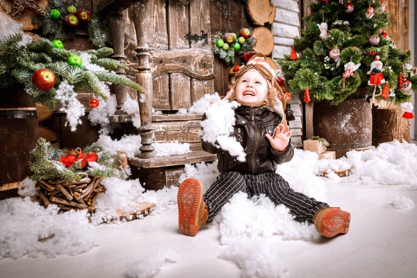 Braun deri ceket, pantolon ve bot üzerinde ahşap dekorasyon kar ile oyunlarında Noel poz pilot şapkası ile küçük iki yaşında bir çocuk giymiş