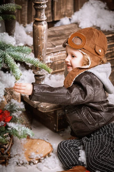 Braun deri ceket, pantolon ve bot üzerinde ahşap dekorasyon kar ile oyunlarında Noel poz pilot şapkası ile küçük iki yaşında bir çocuk giymiş