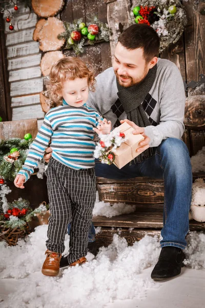 Feliz padre le regala un regalo de Navidad a su hijo en decoraciones con abeto con cajas de regalo y fondo de madera — Foto de Stock