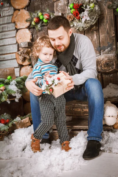 Feliz padre le regala un regalo de Navidad a su hijo en decoraciones con abeto con cajas de regalo y fondo de madera — Foto de Stock