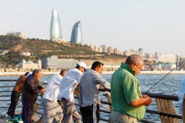 Baku, Azerbaijan - 16 July, 2015: Fishermen on the Caspian Sea against the background of the city of Baku. clipart