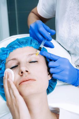 Doktor kozmetik uzmanı güzellik salonundaki kadın cildine Biyolojik Evrimi Yenileme yüz enjeksiyonu prosedürü uyguluyor.