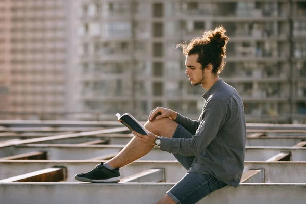 Homem sentado no telhado ler livro e beber chá de café, beber em xícara de papel. Antecedentes das paisagens urbanas. Estilo de vida urbano Fotos De Bancos De Imagens