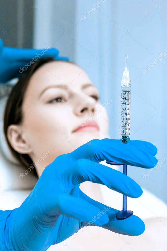 skin care concept. doctor holds a syringe in hand and blue gloves. female patient in a beauty clinic on the background