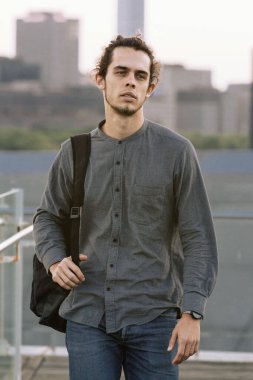 Siyah sırt çantalı bir adam kameraya doğru yürüyor. Şehir manzaralarının arka planı. Kentsel yaşam tarzı seyahat kavramı