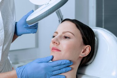 Estetik ameliyattan önce cilt kontrolü. Güzellik uzmanı kadın yüzüne dokunuyor.