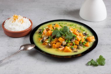 Bezelye, maydanoz, bir kase pilav ve beyaz bir vazo ile siyah bir tabakta ile tepesinde ile tatlı patates köri.