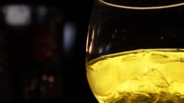 Barmen bir cam - sarı içki siyah arka plan üzerine bir buz küpü koymak 