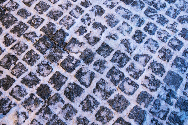 The texture of paving stone masonry sprinkled with snow, close up.