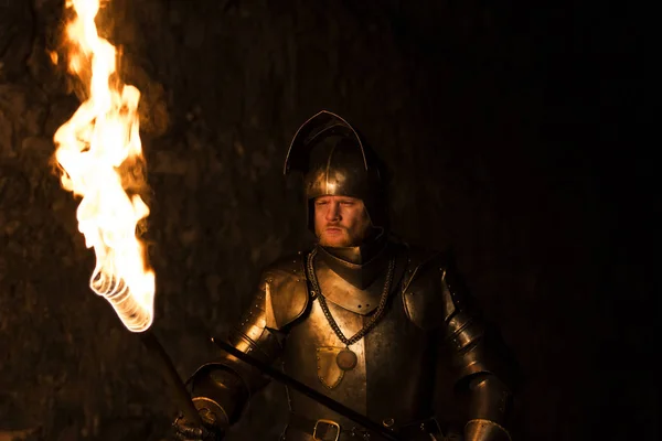 Рыцарь с факелом и мечом ночью на фоне стены — стоковое фото