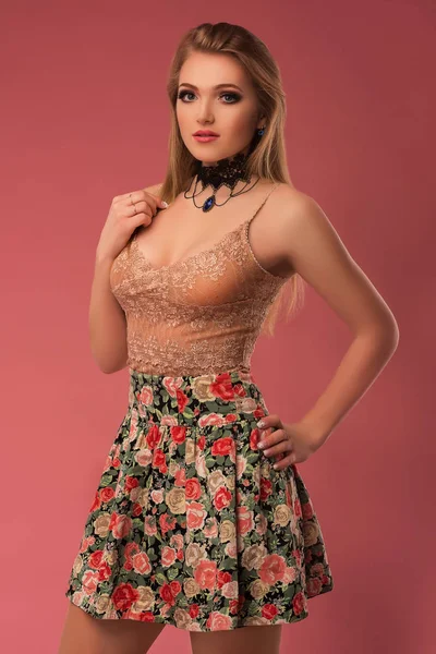 Modefoto einer schönen jungen Frau in einem hübschen Kleid mit Blumen posiert auf dem rosa Hintergrund. Modefoto — Stockfoto