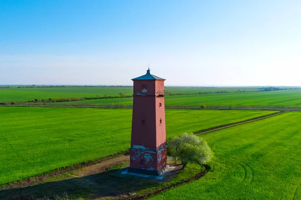 Old lighthouse with red stripes in spring field. Scenic landscape with a tall lighthouse.