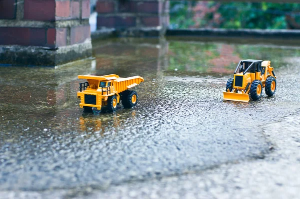 İki sarı oyuncak forklines bahar yağmur sonrası biraz su ile bahçede oynuyorlar.