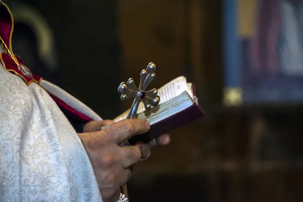Salib perak dengan perhiasan merah dan Alkitab Suci di tangan imam laki-laki yang mengenakan jubah emas pada upacara di gereja katedral kristen, acara sakramen suci. Yerevan, Armenia — Stok Foto
