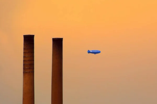 New York, Verenigde Staten - augustus 09, 2012: blauwe luchtschip reclame directv in het avondrood met twee schoorstenen silhouetten — Stockfoto