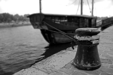 Rusted mooring bollard with ropes on the berth. Moored tourist boat in the blurred background. River Seine, Paris, France. black and white photography clipart