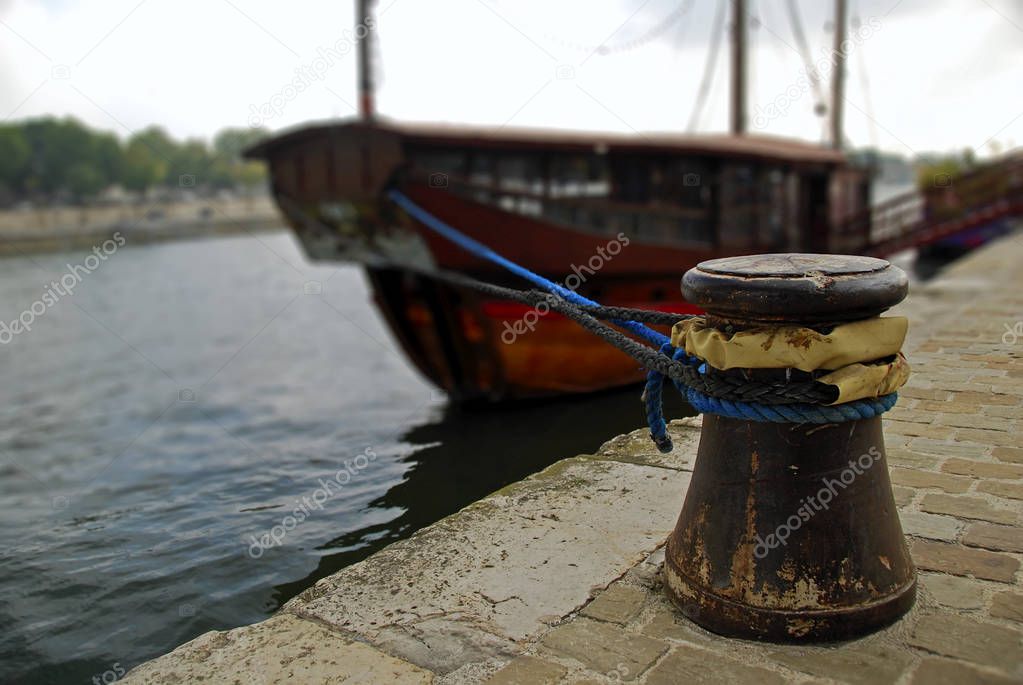 Rusted mooring bollard with ropes on the berth. Moored tourist boat in the blurred background. River Seine, Paris, France