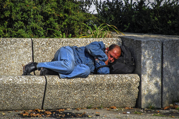 Paris, France - September 23, 2008: The homeless man is sleeps on a stone bench in a city park. street photography  