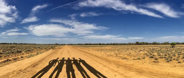 Sombras de gente parada en el camino de la suciedad por campo de la granja contra cielo azul con nubes — Foto de Stock