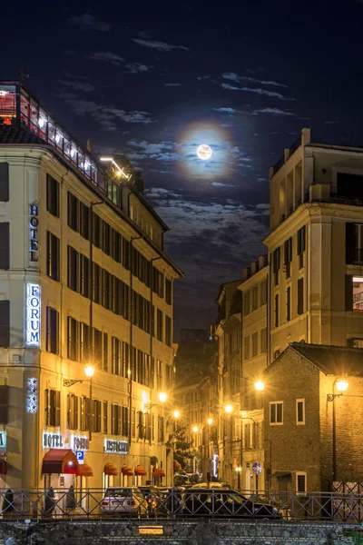 Roma, Italia - 16 de noviembre de 2016: Luna vista a través de las nubes sobre el "Forum" Hotel iluminado por la noche. Hermoso paisaje urbano nocturno adecuado para fondos . — Foto de Stock