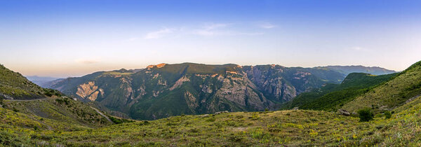 wide panorama of mountains slopes at Vorotan river canyon lit by sunset sunlight, view from Halidzor village, Syunik Province, Armenia