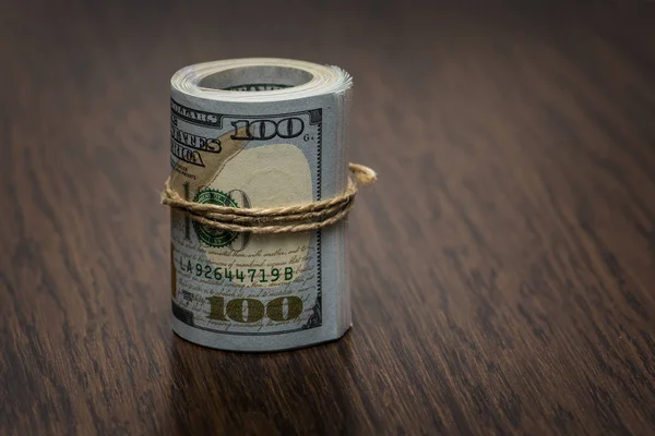 Detalhe macro de um rolo de moeda americana (USD, dólares americanos) com notas bancárias de 100 e 50 dólares do lado de fora como um símbolo de muito dinheiro no fundo de madeira. Dinheiro na mesa — Fotografia de Stock