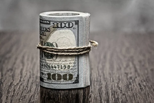 Macro detail of a roll of American currency (USD, American dollars) with 100 and 50 dollars bank notes on the outside as a symbol of plenty of money on the wooden background. Vintage/retro color style