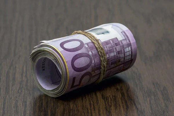 Detalle macro de un rollo de euro moneda (EUR) con billetes de banco de 500, 200, 100 y 50 euros en el exterior como símbolo de un montón de dinero en el fondo de madera. Dinero sobre la mesa — Foto de Stock