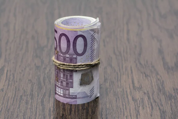 Detalle macro de un rollo de euro moneda (EUR) con billetes de banco de 500, 200, 100 y 50 euros en el exterior como símbolo de un montón de dinero en el fondo de madera. Dinero sobre la mesa — Foto de Stock
