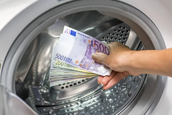 Nahaufnahme einer Person, die schmutziges Geld in die Waschmaschine steckt. Eurowährung (Euro) mit 500, 200, 100 und 50-Euro-Banknoten — Stockfoto