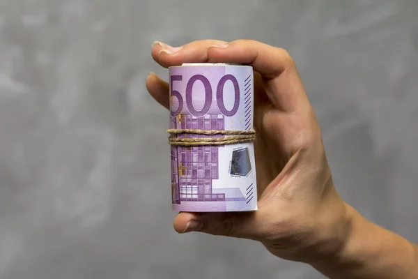 Detalle macro de un rollo de euro moneda (EUR) con billetes de banco de 500 euros en una mano de mujer sobre fondo gris — Foto de Stock