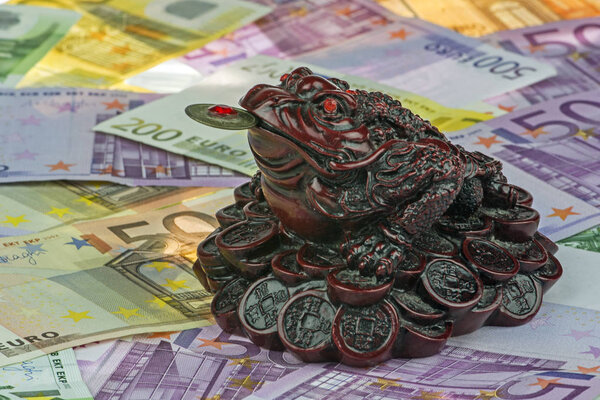 three-legged money toad Jin Chan as a chinese symbol of wealth on variety of Euro currency (EUR) with 500, 200, 100 and 50 euro bank notes.  Many money. Euro background.