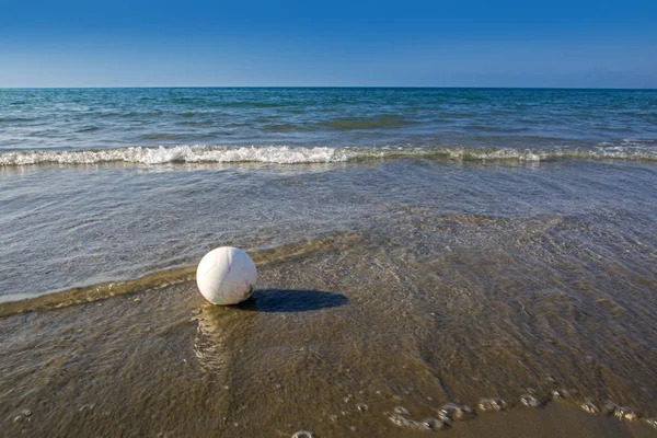 Bola branca na água na praia faz sombra contra o fundo azul do mar e do céu — Fotografia de Stock