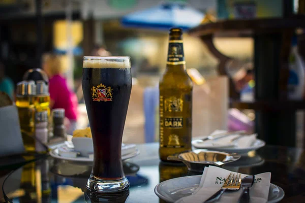 Korfu, Grecja - 26 sierpnia 2017: Zimną Kubek ciemnego piwa grecki na stół szkło przed niewyraźne tło — Zdjęcie stockowe