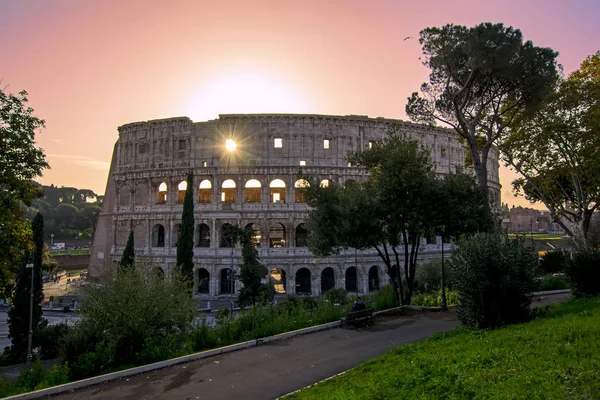 Belo pôr do sol com o sol brilhando através de uma das janelas do Coliseu em Roma, Itália. amantes em um banco de parque — Fotografia de Stock