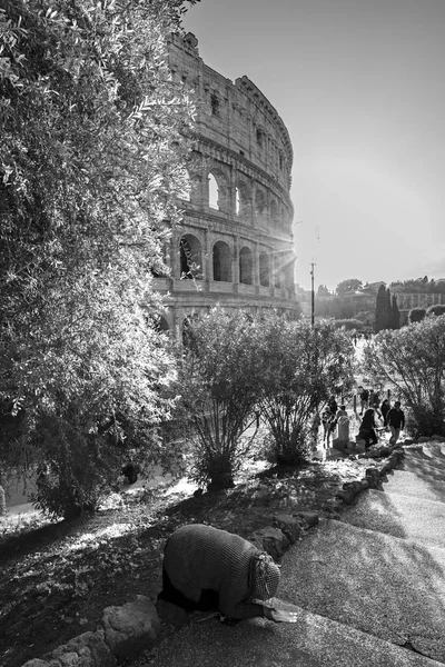 Una scena commovente con una mendicante su un marciapiede davanti al Colosseo di Roma. Fotografia verticale in bianco e nero — Foto Stock