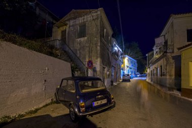 Karousades, Corfu, Yunanistan - 31 Ağustos 2017: gece cityscape lacivert Austin Mini Cooper 1000 antika evleriyle dar sokakta ile eski Akdeniz Köyü 