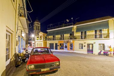 Karousades, Corfu, Yunanistan - 31 Ağustos 2017: gece cityscape antika evleri, Ortodoks Kilisesi ve kırmızı araba ile eski Akdeniz köyü. Uzun pozlama