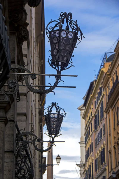 Vertical cityscape with the row of vintage metal streetlights and Obelisco Sallustiano on blurred background in Rome, Italy