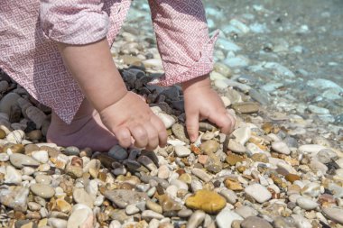Masmavi denizin önünde sahilde küçük çakıl taşları üzerinde çocuk Close-up eller. Yeni yaşam konsepti