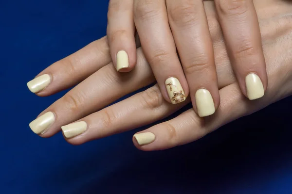 Beautiful female finger nails with beige nail closeup on petals. Perfect cream manicure with golden drawing. Woman hands with manicure beige nails closeup on dark blue background. Skin and nail care