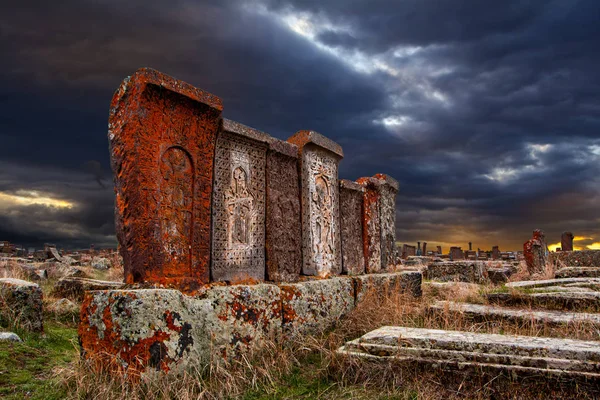Ancient tombstones known as Khachkars covered with moss and lichen in the Historical cemetery of Noratus in Armenia, near the Lake Sevan under the beautiful dramatic sunset sky. 10th century