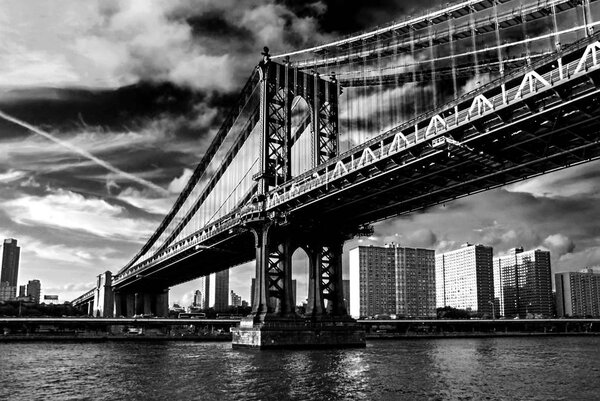 Famous Manhattan Bridge in New York City, USA with financial district, downtown Manhattan in background. East River and beautiful sunset reflection. Black and white photography, low angle view