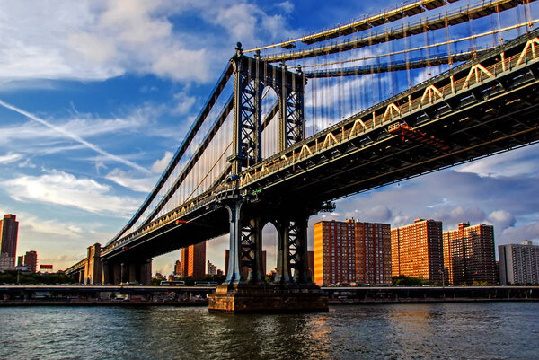 Famous Manhattan Bridge in New York City, USA with financial district, downtown Manhattan in background. East River and beautiful sunset reflection. Low angle view